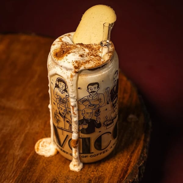 A drink in a decorated can, topped with whipped cream, cinnamon, a cookie, and a glass straw.