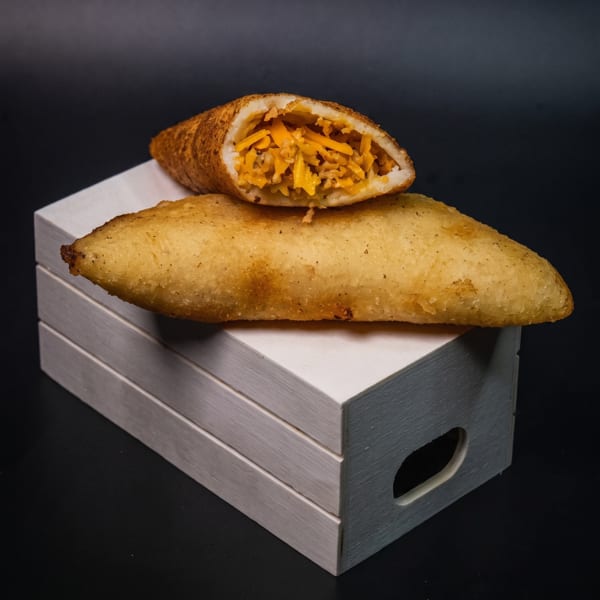 Two golden-brown empanadas, one sliced open to reveal a cheesy filling, rest on a white wooden box.