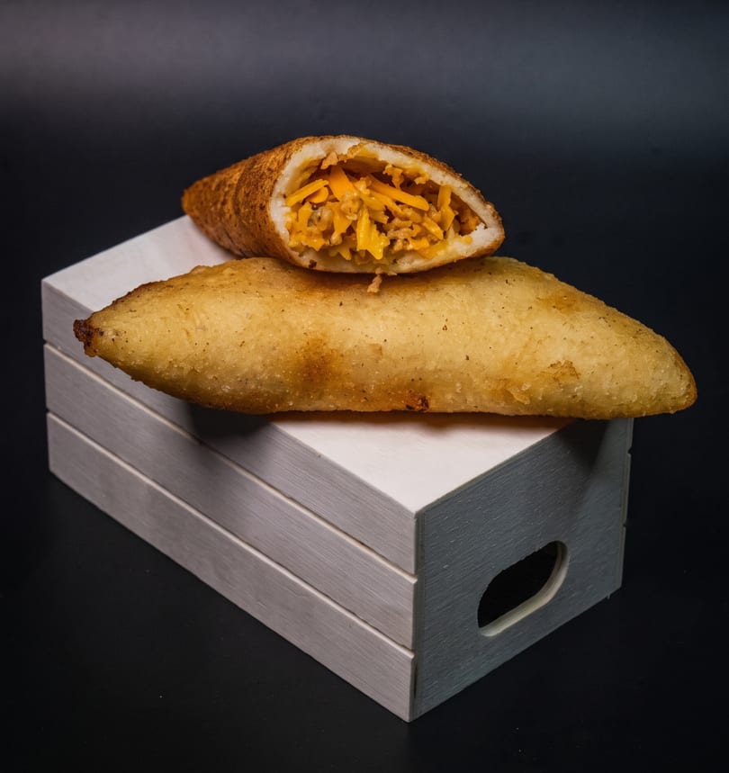 Two golden-brown empanadas, one sliced open to reveal a cheesy filling, rest on a white wooden box.