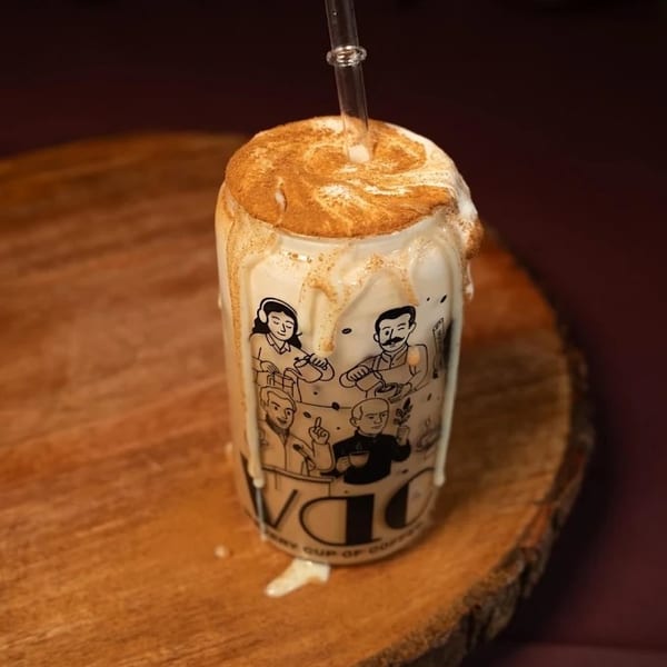 A tall glass of iced coffee with whipped cream, cinnamon, and a straw on a wooden slab.