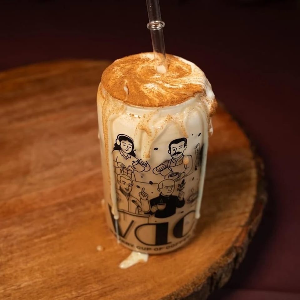 A tall glass of iced coffee with whipped cream, cinnamon, and a straw on a wooden slab.