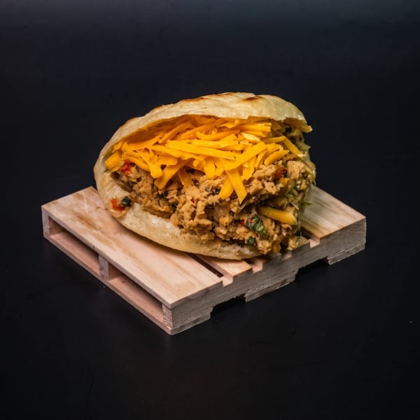 A stuffed arepa with shredded chicken and cheese, resting on a small wooden pallet.