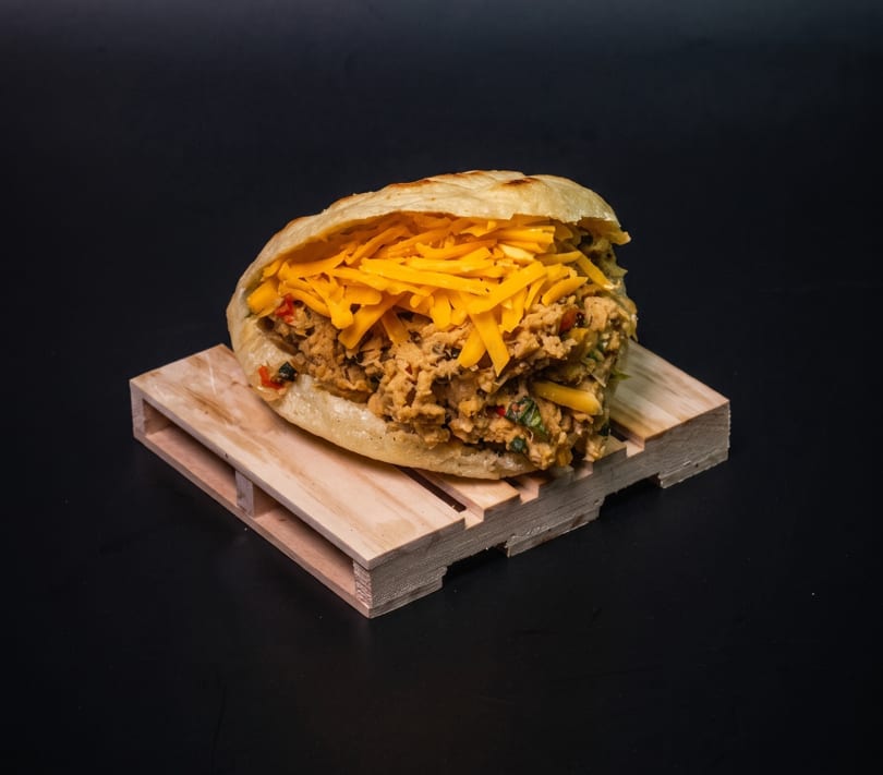 A stuffed arepa with shredded chicken and cheese, resting on a small wooden pallet.