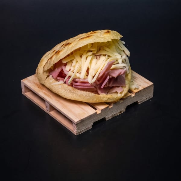 Arepa filled with shredded white cheese and sliced ham, served on a miniature wooden pallet.
