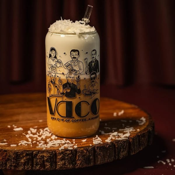 A Vaco branded glass with a layered drink, topped with whipped cream and coconut flakes.